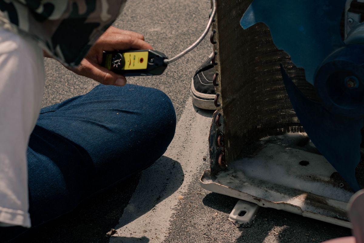Technician testing an air conditioning unit's electrical circuit with a multimeter.